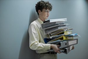 A young worker holding lots of documents in hands illustrating bad work culture - Bureaucracy